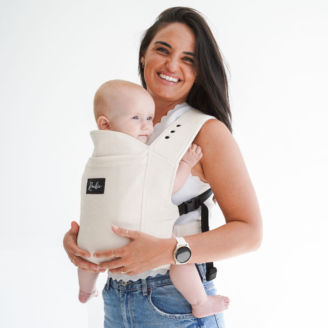 Woman smiling, wearing a baby in a black carrier.